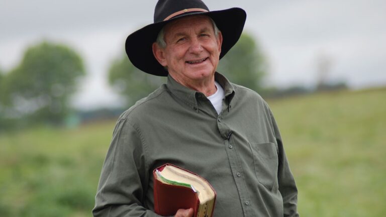 Angus Buchan standing in a field with a Bible under his arm