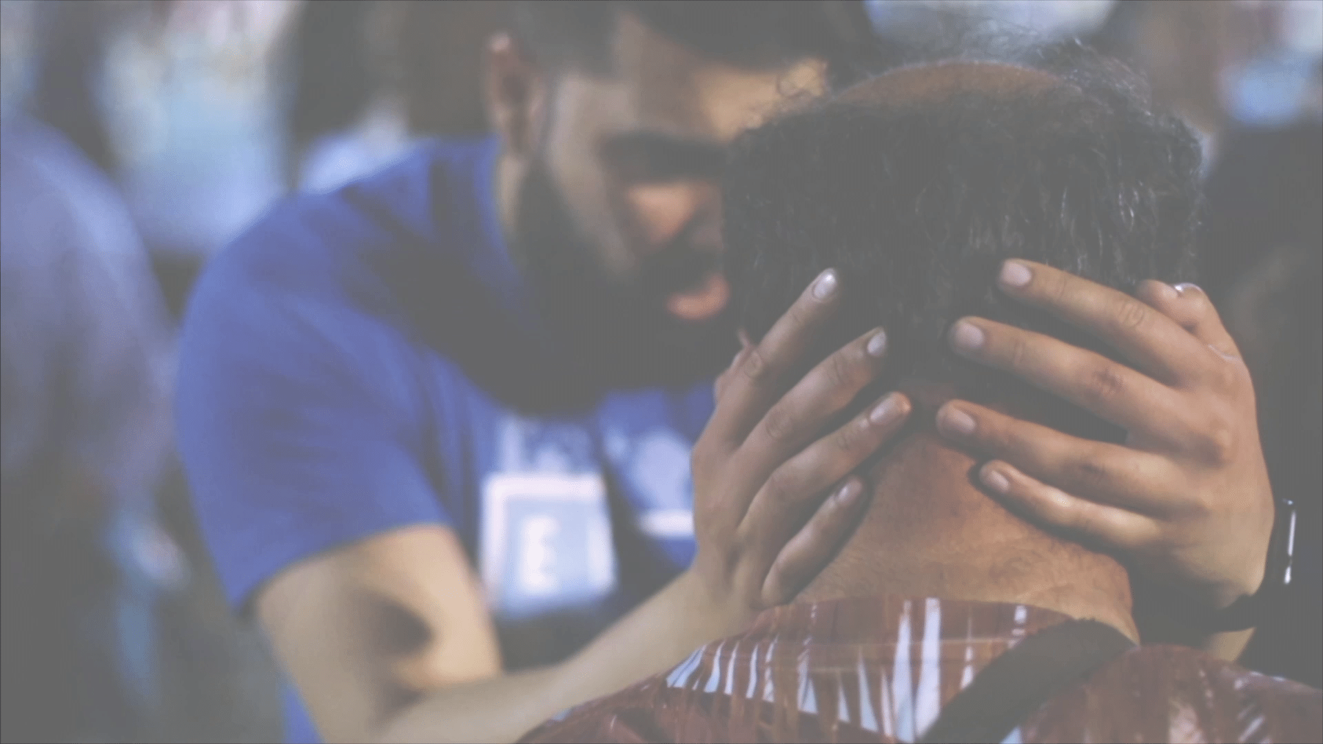 A man lays hands on another man's head, praying for him