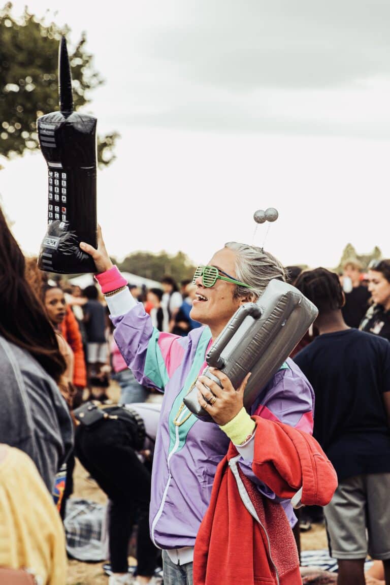 A woman wearing a fun festival outfit and carrying an inflatable phone