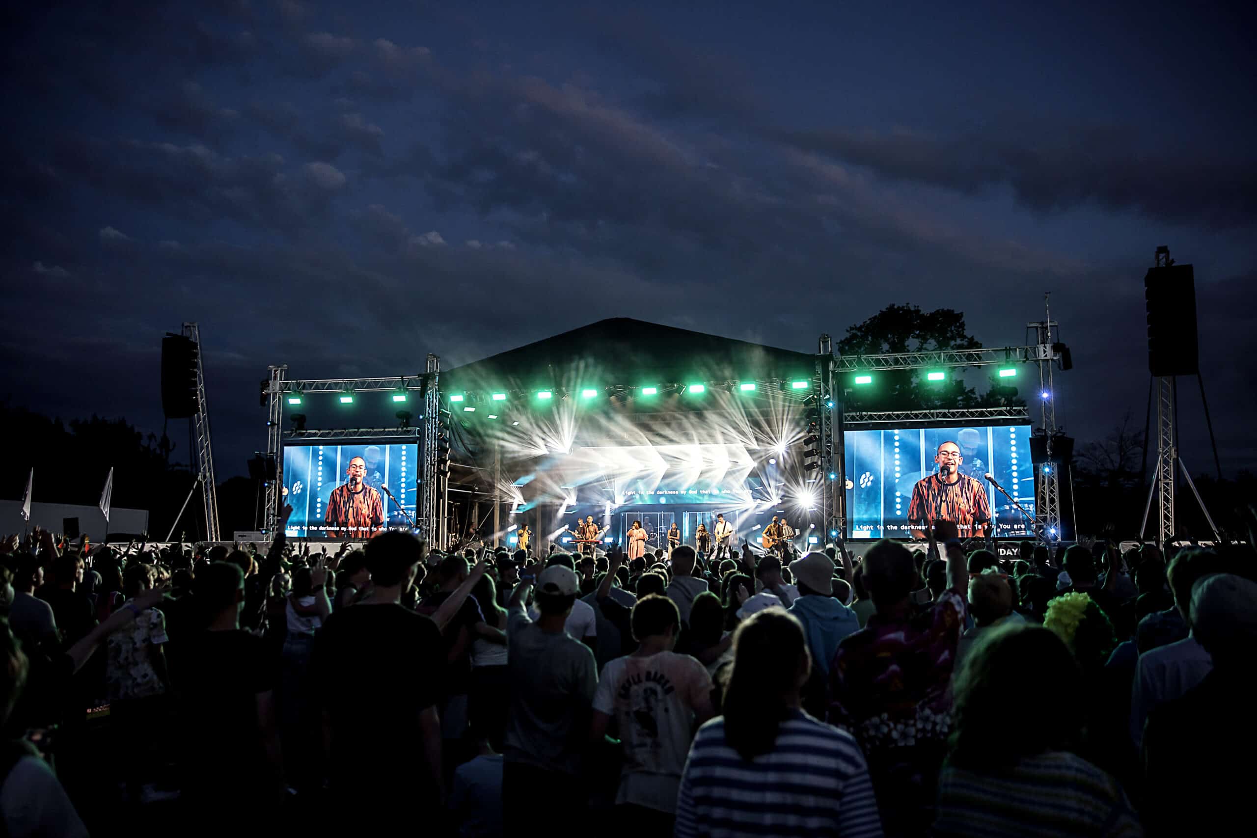 Crowd of thousands stand in front of a lit stage at Newday, worshipping God together