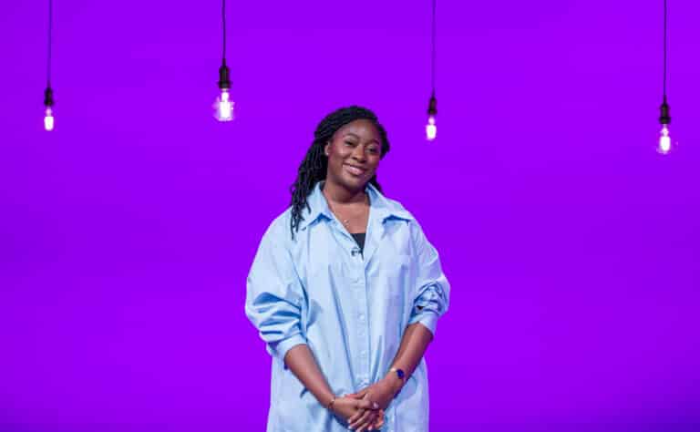 Kika Ashanike in front of a purple background with some hanging lights