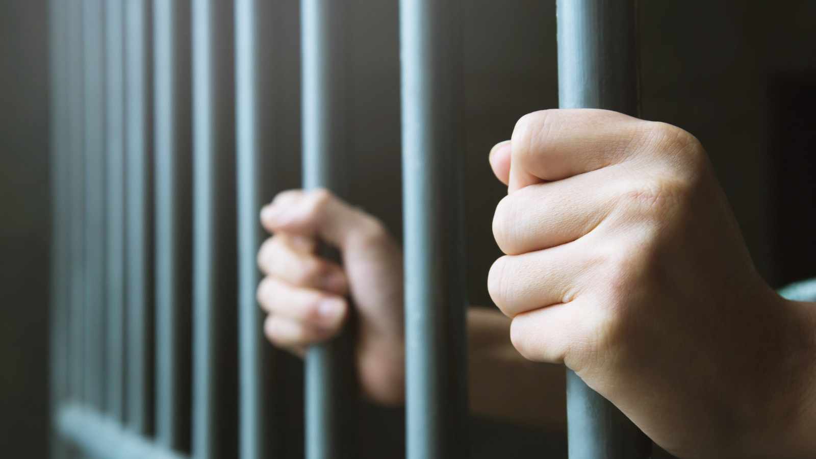 Man behind bars - hands holding prison bars